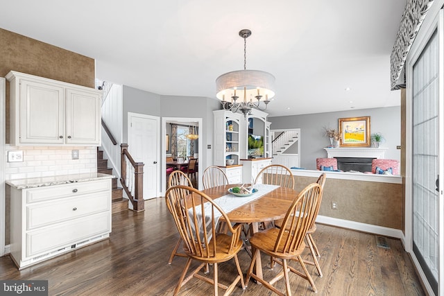 dining room featuring dark wood-style flooring, a fireplace, a chandelier, baseboards, and stairs