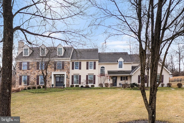 view of front of property featuring a front yard, stone siding, and a chimney