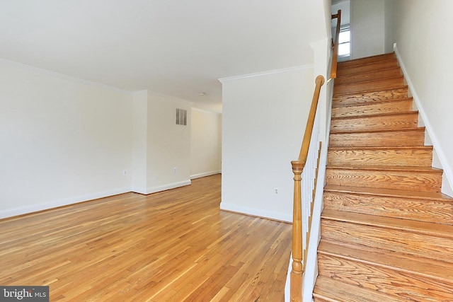 staircase featuring visible vents, baseboards, crown molding, and wood finished floors