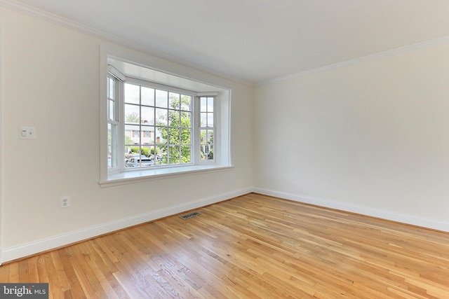 spare room featuring crown molding, baseboards, light wood finished floors, and visible vents