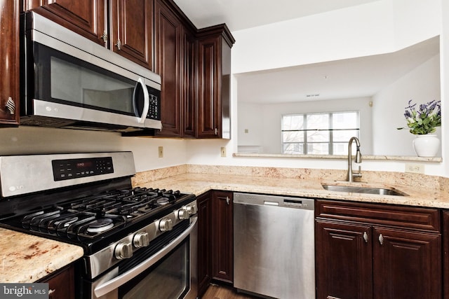 kitchen featuring stainless steel appliances, sink, light stone counters, and dark brown cabinetry