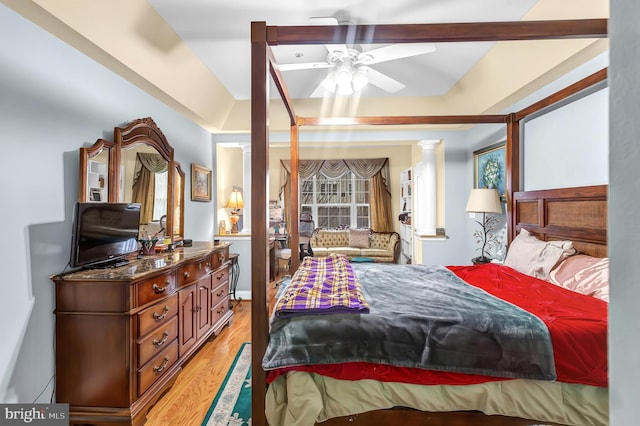 bedroom featuring a tray ceiling, light hardwood / wood-style floors, decorative columns, and multiple windows