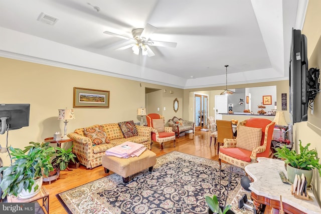 living room with hardwood / wood-style flooring, a raised ceiling, and ceiling fan