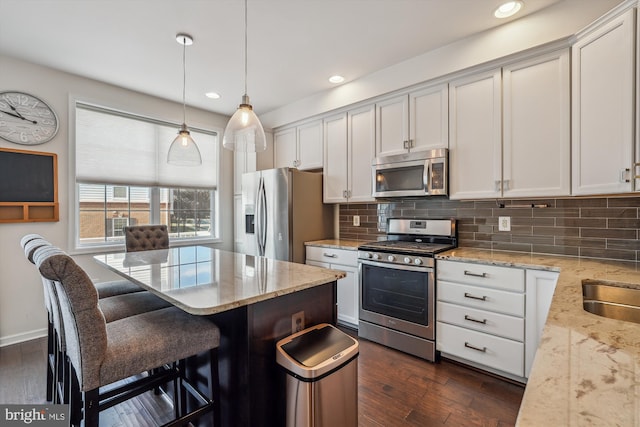 kitchen featuring decorative light fixtures, a kitchen bar, decorative backsplash, light stone counters, and stainless steel appliances