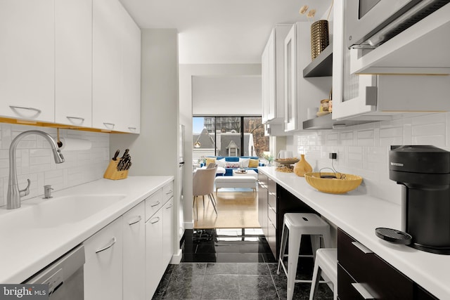 kitchen featuring a sink, decorative backsplash, granite finish floor, and white cabinetry