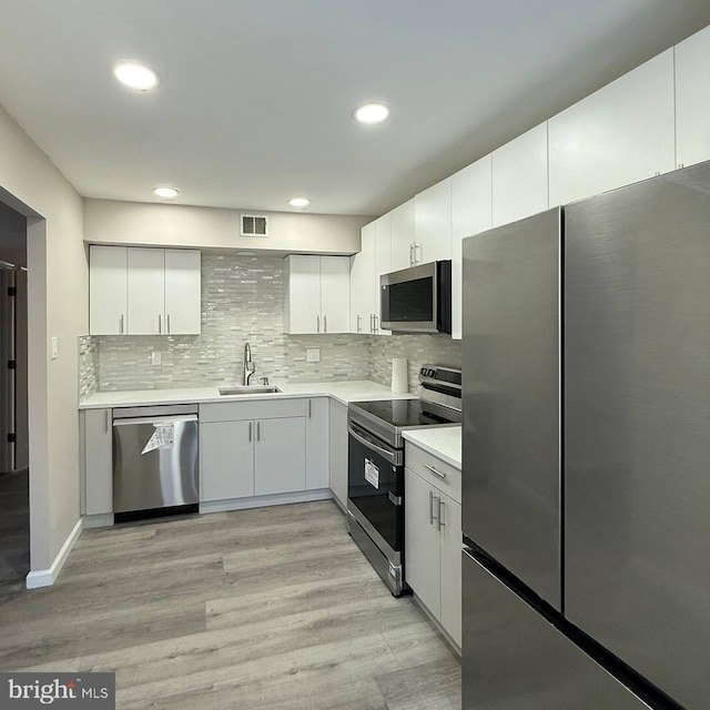 kitchen with sink, tasteful backsplash, light hardwood / wood-style flooring, stainless steel appliances, and white cabinets