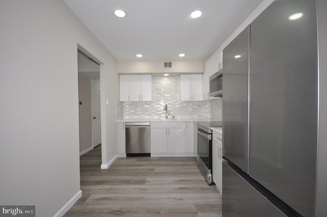 kitchen featuring appliances with stainless steel finishes, tasteful backsplash, white cabinetry, sink, and light hardwood / wood-style floors