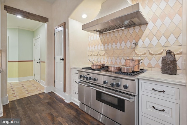 kitchen with a wainscoted wall, light countertops, wall chimney range hood, and stainless steel range