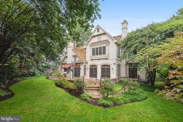 back of property featuring french doors, a lawn, a chimney, and stucco siding