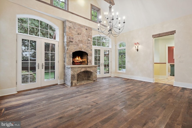 unfurnished living room with a towering ceiling, dark wood-type flooring, a stone fireplace, and french doors