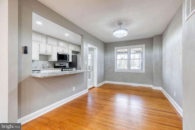 kitchen with appliances with stainless steel finishes, white cabinets, light stone counters, and light hardwood / wood-style flooring