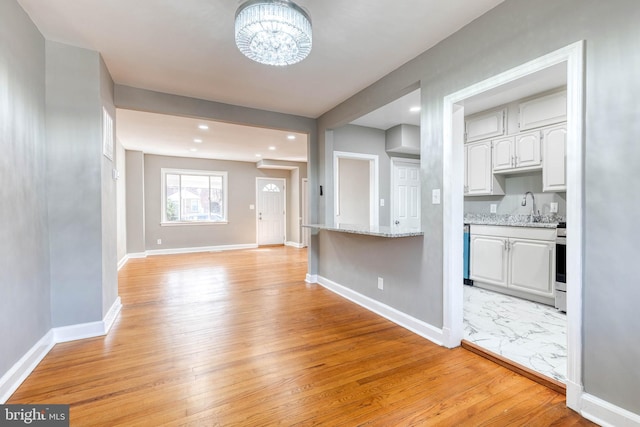 kitchen featuring white cabinetry, sink, light hardwood / wood-style floors, light stone countertops, and stainless steel range oven