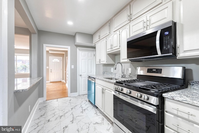 kitchen featuring stainless steel appliances, white cabinetry, sink, and light stone counters