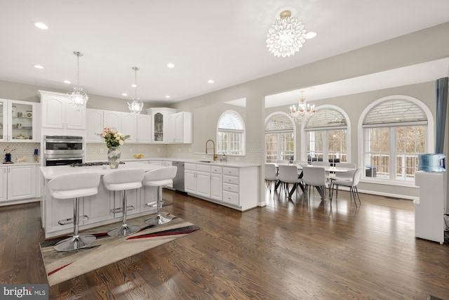 kitchen featuring glass insert cabinets, appliances with stainless steel finishes, light countertops, white cabinetry, and a notable chandelier