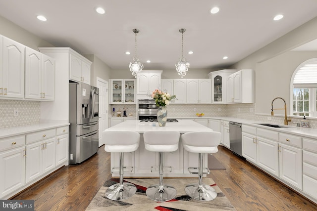 kitchen featuring appliances with stainless steel finishes, a kitchen bar, a sink, and glass insert cabinets