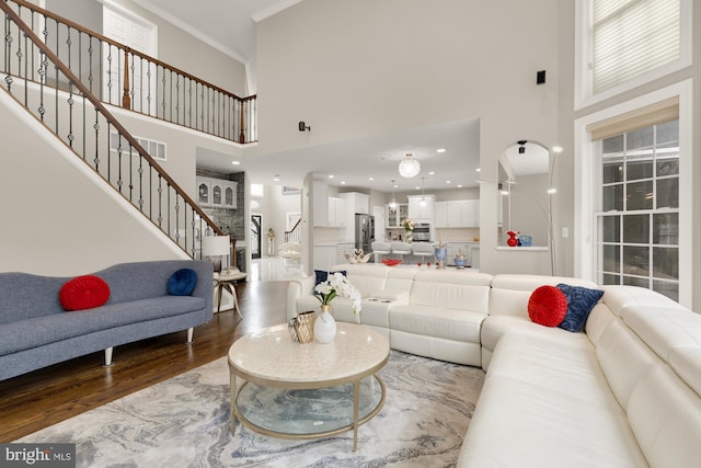 living area featuring crown molding, visible vents, a high ceiling, wood finished floors, and stairs