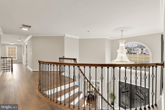 hall featuring visible vents, ornamental molding, hardwood / wood-style floors, an upstairs landing, and a notable chandelier