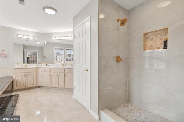 full bath with double vanity, tiled shower, a sink, and visible vents