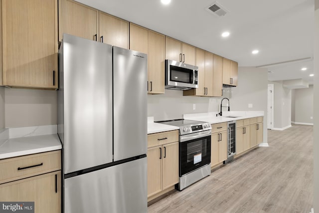 kitchen featuring light wood finished floors, wine cooler, stainless steel appliances, light brown cabinetry, and a sink