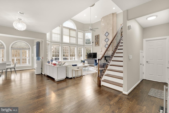 living room with baseboards, a towering ceiling, stairway, wood finished floors, and ceiling fan with notable chandelier