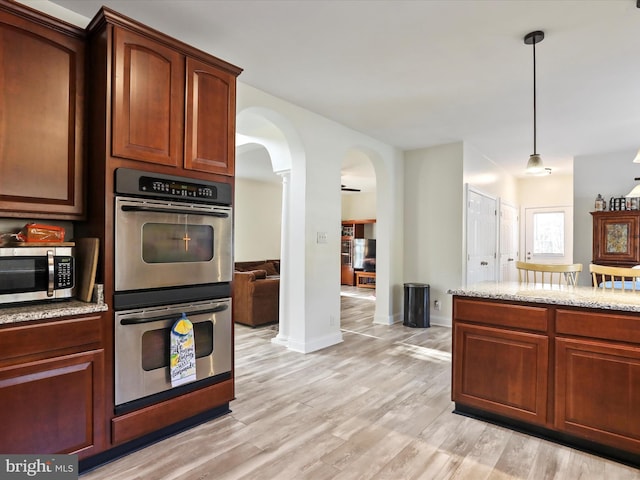 kitchen with stainless steel appliances, pendant lighting, light stone counters, and light wood-type flooring