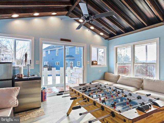 rec room with a healthy amount of sunlight, sink, light hardwood / wood-style floors, and lofted ceiling with beams