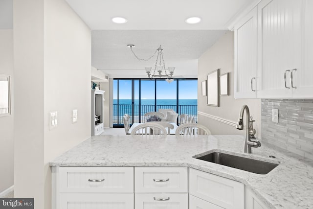 kitchen with sink, a water view, white cabinetry, tasteful backsplash, and light stone counters