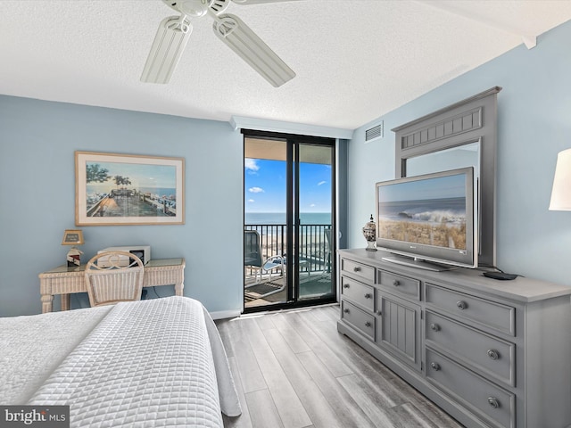 bedroom with a wall of windows, ceiling fan, access to exterior, light hardwood / wood-style floors, and a textured ceiling