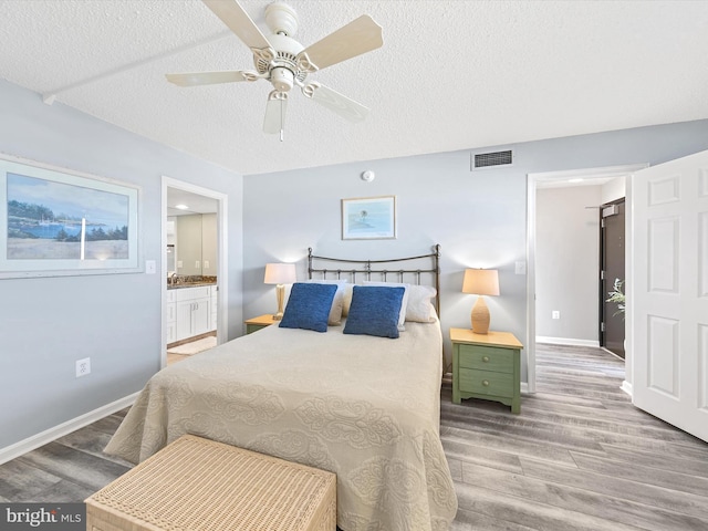 bedroom with ceiling fan, ensuite bath, hardwood / wood-style floors, and a textured ceiling