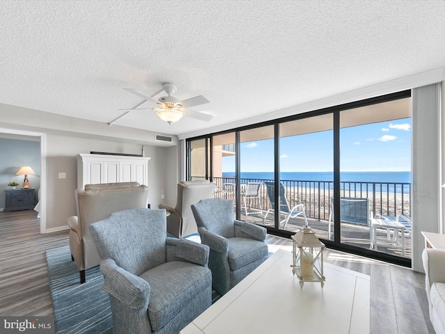 living room featuring ceiling fan, a water view, wood-type flooring, expansive windows, and a textured ceiling