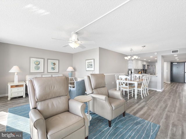 living room featuring ceiling fan with notable chandelier, hardwood / wood-style floors, and a textured ceiling