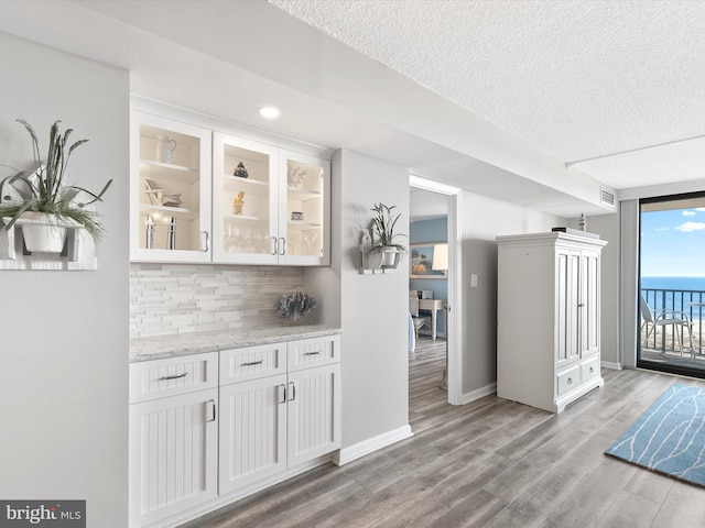 bar featuring tasteful backsplash, light stone counters, white cabinets, and light wood-type flooring