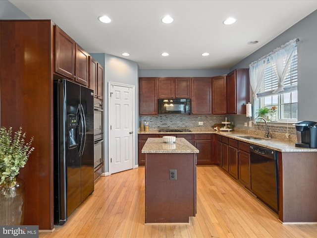 kitchen featuring sink, a center island, light wood-type flooring, decorative backsplash, and black appliances