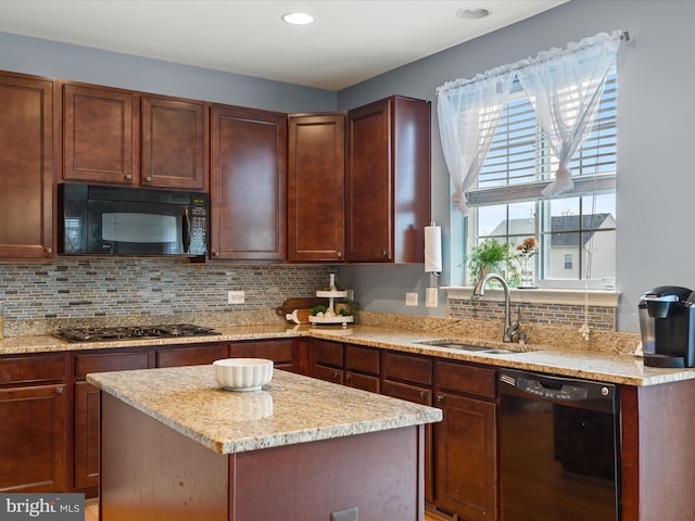 kitchen with sink, tasteful backsplash, a center island, light stone countertops, and black appliances