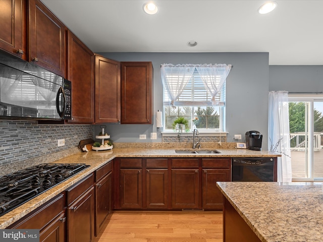 kitchen with sink, backsplash, light stone counters, black appliances, and light wood-type flooring