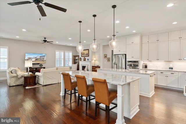 kitchen with stainless steel appliances, a breakfast bar, white cabinetry, a large island with sink, and pendant lighting