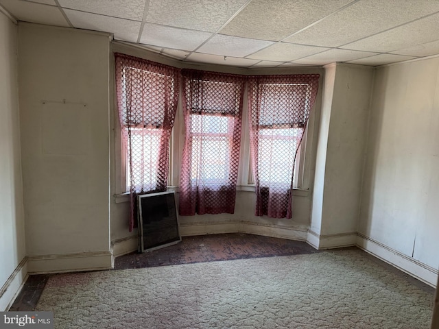 empty room with carpet floors, a wealth of natural light, and a drop ceiling