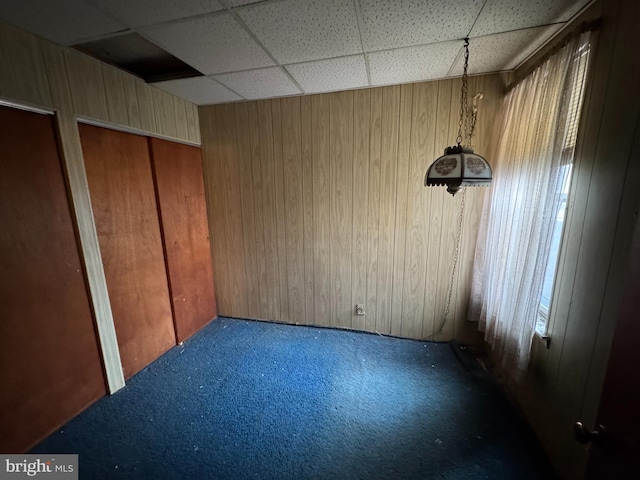 unfurnished bedroom with carpet flooring, a drop ceiling, and wood walls