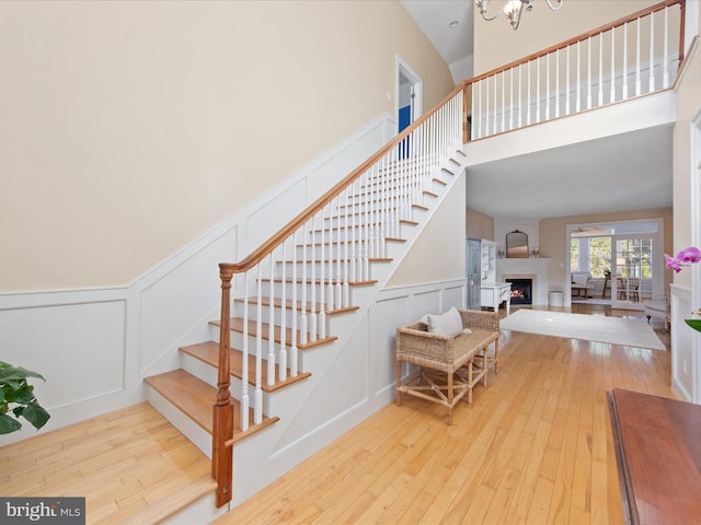 stairway with a towering ceiling, wood-type flooring, a large fireplace, and a chandelier