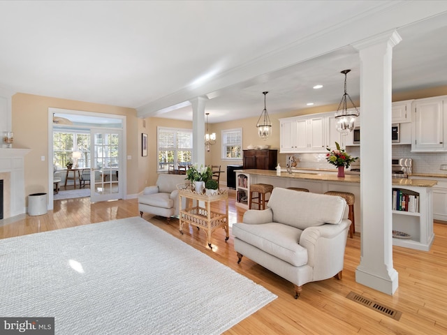 living room with an inviting chandelier, sink, light hardwood / wood-style floors, and decorative columns