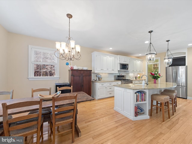 kitchen with pendant lighting, appliances with stainless steel finishes, light stone countertops, white cabinets, and a center island with sink