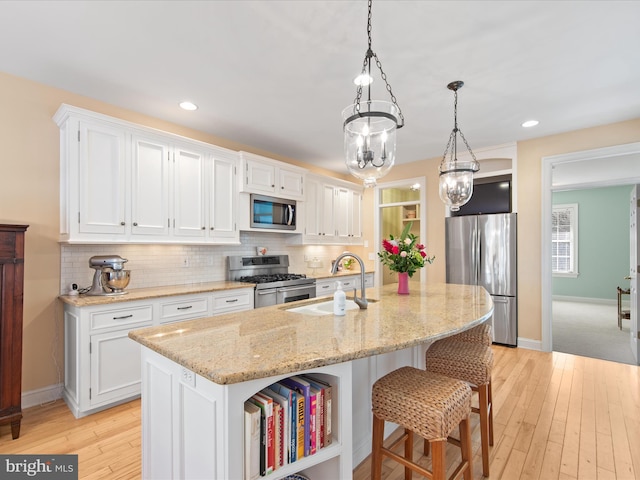 kitchen with white cabinetry, sink, a kitchen island with sink, stainless steel appliances, and light stone countertops