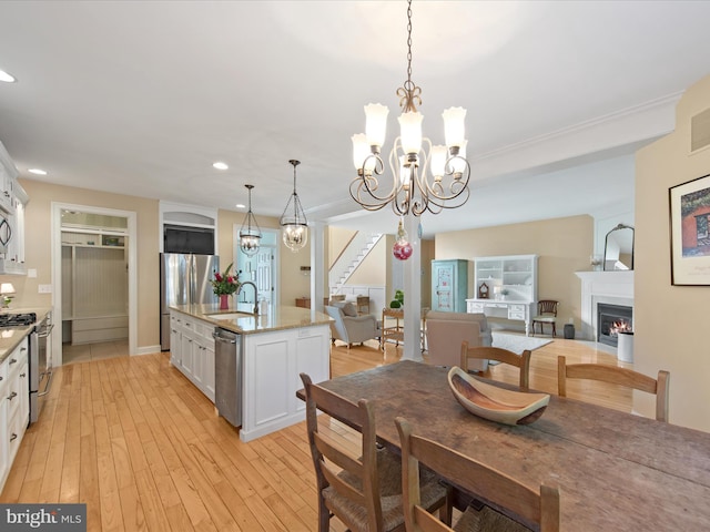 dining area with an inviting chandelier, sink, and light hardwood / wood-style flooring