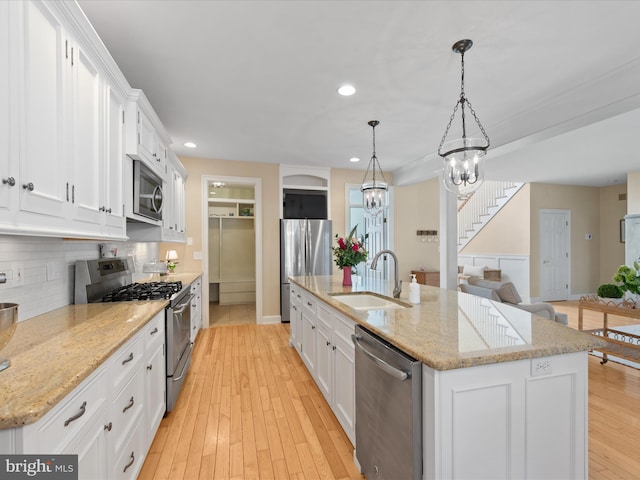 kitchen featuring an island with sink, sink, white cabinets, hanging light fixtures, and stainless steel appliances