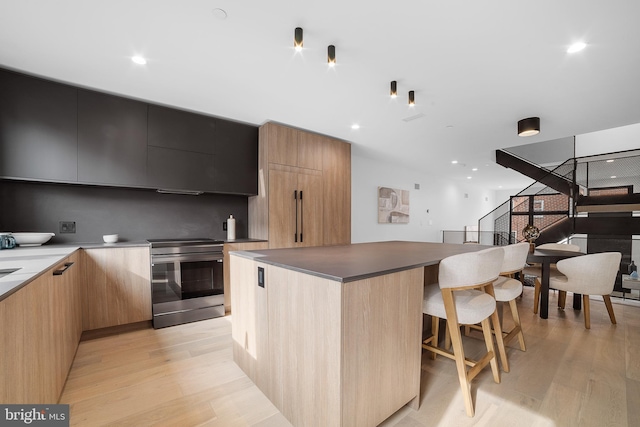 kitchen with stainless steel electric stove, light hardwood / wood-style floors, a breakfast bar area, and a kitchen island