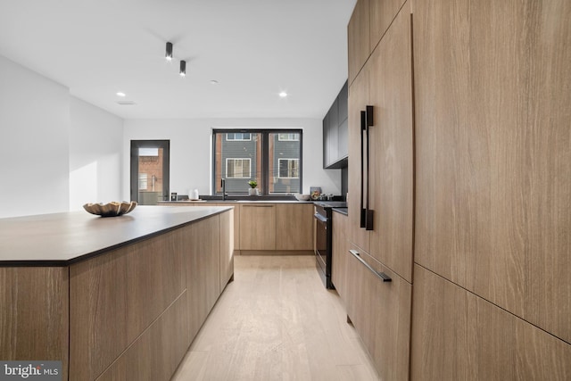 kitchen with sink, light hardwood / wood-style flooring, stove, a kitchen island, and light brown cabinetry