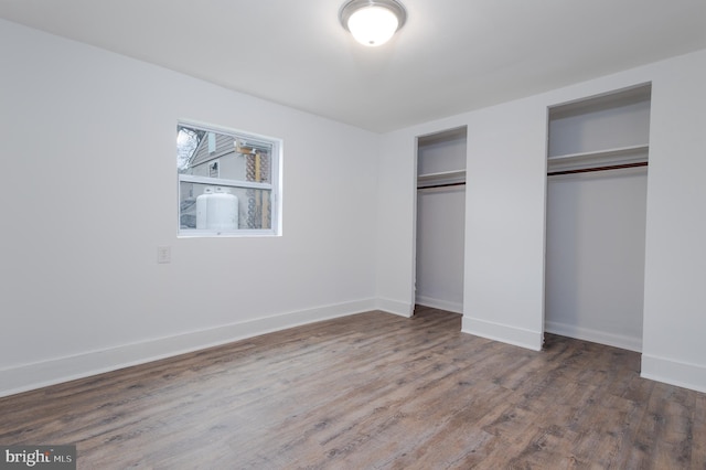 unfurnished bedroom with dark hardwood / wood-style flooring and two closets