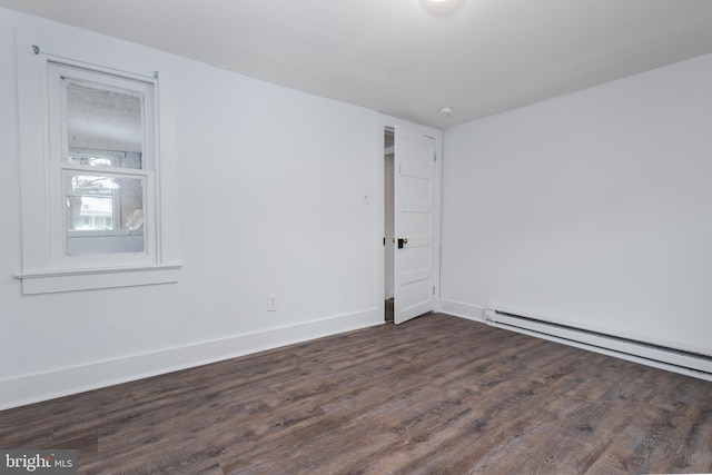 spare room featuring baseboard heating and dark hardwood / wood-style flooring