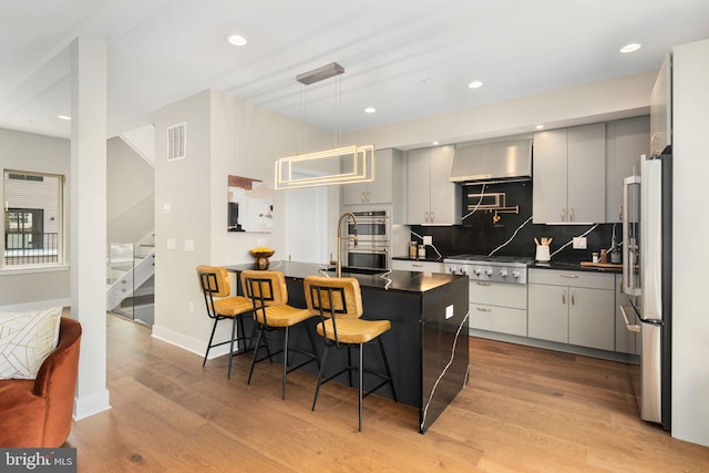 kitchen with a kitchen bar, appliances with stainless steel finishes, gray cabinets, pendant lighting, and light hardwood / wood-style floors