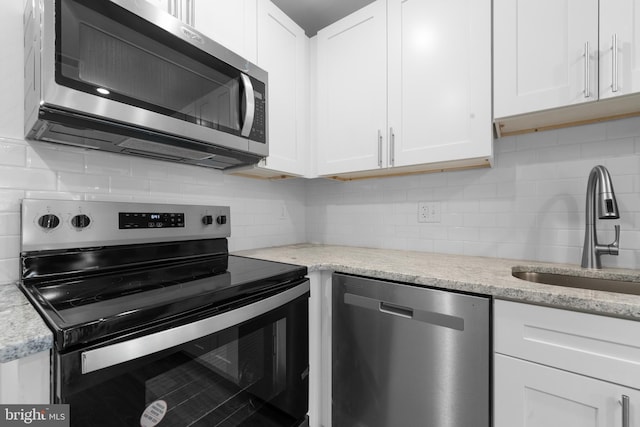 kitchen with sink, appliances with stainless steel finishes, white cabinetry, backsplash, and light stone countertops